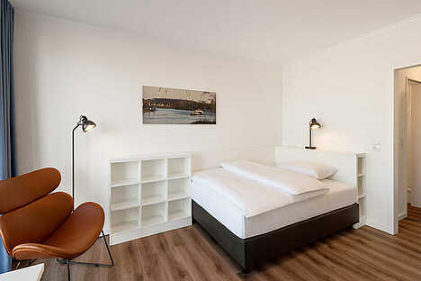 Schlafbereich eines Apartments mit einem Boxspringbett und ein weißes Regal